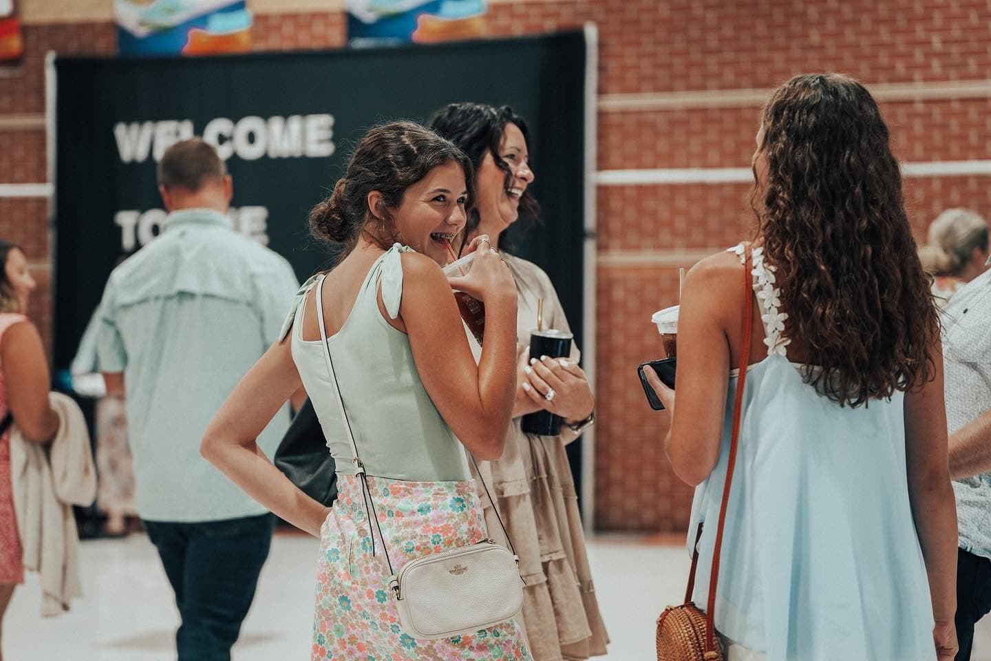 Friends laughing together with iced drinks in the lobby, in front of a Welcome banner